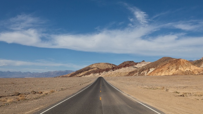 Desert road leading to colorful mountains under a blue sky