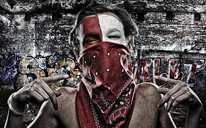 Man with bandana and face paint in front of graffiti wall