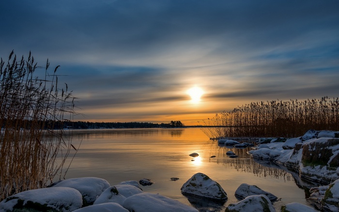 Winter Sunrise Over Calm Lake with Snowy Rocks and Reeds