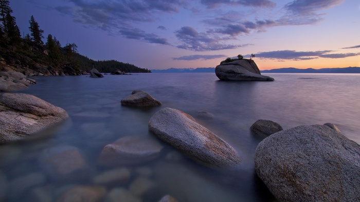 Rocky lake shore at twilight with distant mountains