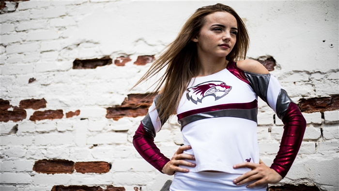 Cheerleader in uniform posing against brick wall
