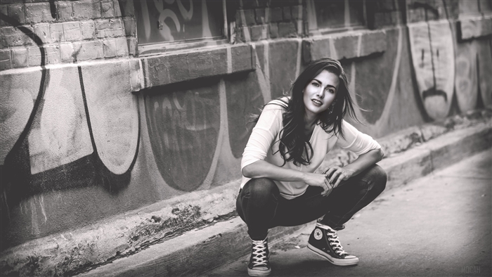 Girl crouching in front of graffiti wall, monochrome 4K