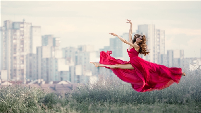 Woman in red dress dancing in front of city buildings