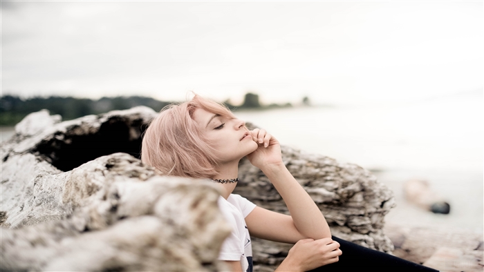 Blonde girl sitting on rocks by the sea 4K