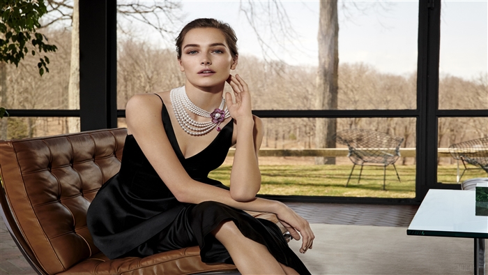Woman in black dress wearing pearl necklace on sofa 4K
