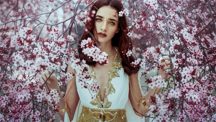 Woman in white and gold dress surrounded by pink blossoms