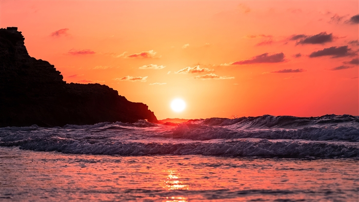 Sunset over ocean waves with rocky cliff