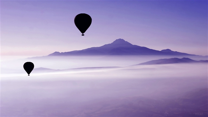 Two hot air balloons over misty mountains