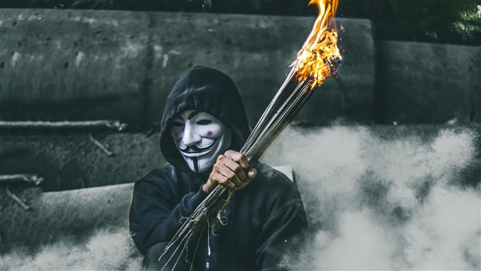 Guy in Guy Fawkes mask holding burning bundle