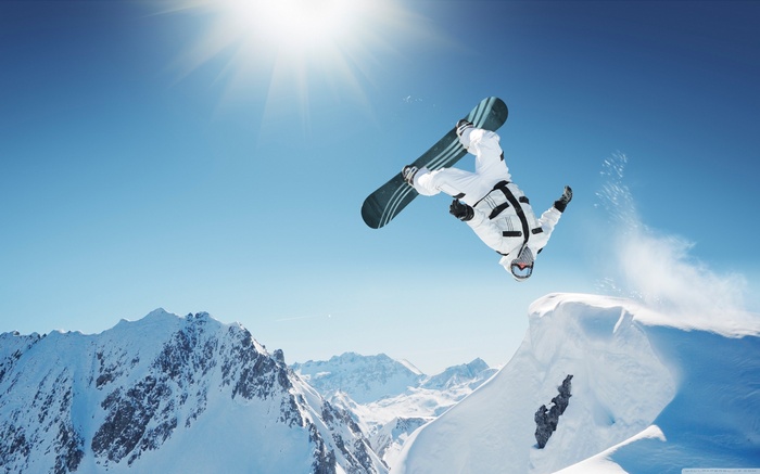 Snowboarder performing a flip over a snowy mountain jump