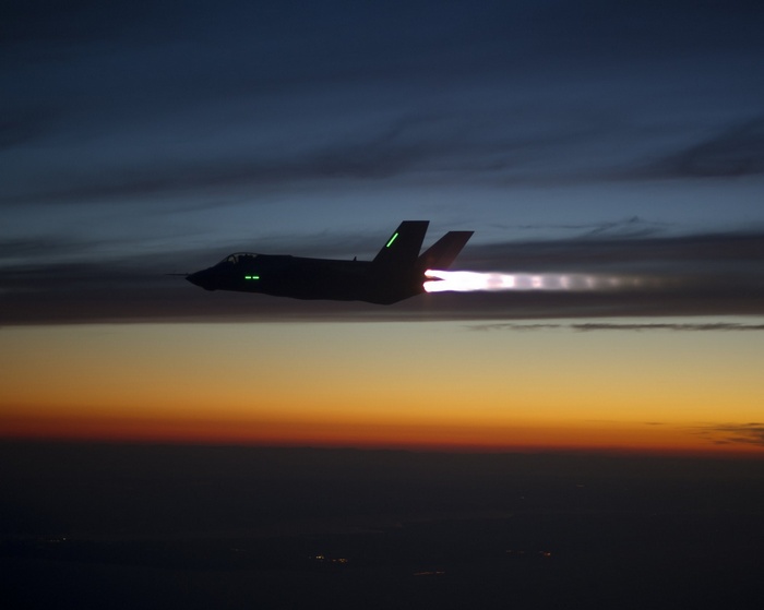 F-35 fighter jet flying at dusk with afterburners on