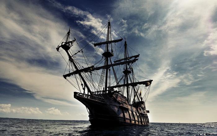 Silhouette of a tall ship sailing on the ocean under a cloudy sky