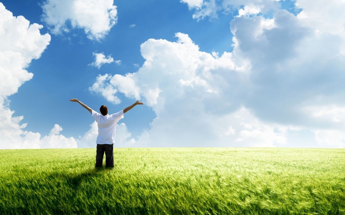 Man with arms outstretched in a green field under a blue sky with clouds