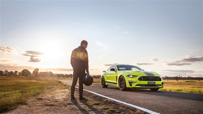 Man with helmet and yellow Ford Mustang on road