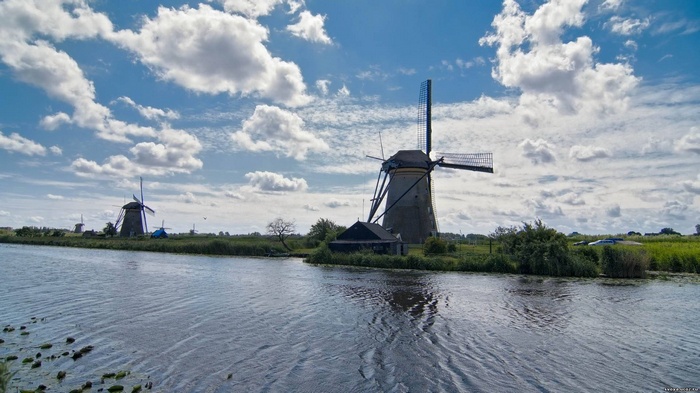 Windmills along a canal under a cloudy sky