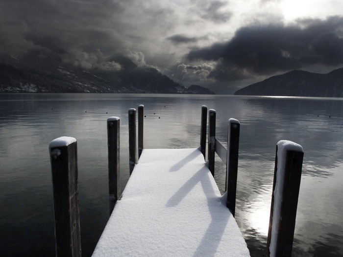 Snowy dock on a lake with mountains and stormy clouds