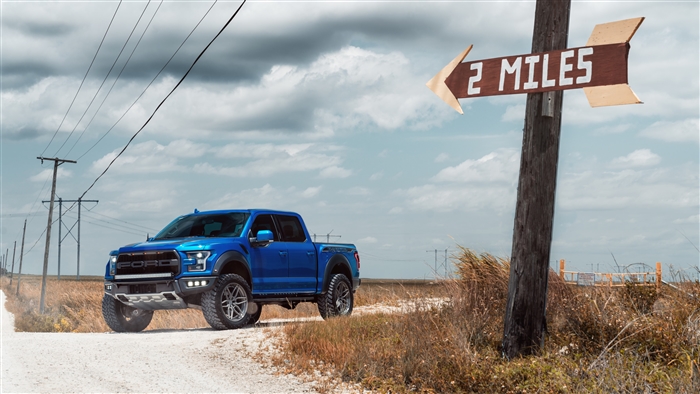Blue Ford Raptor on a dirt road with a sign