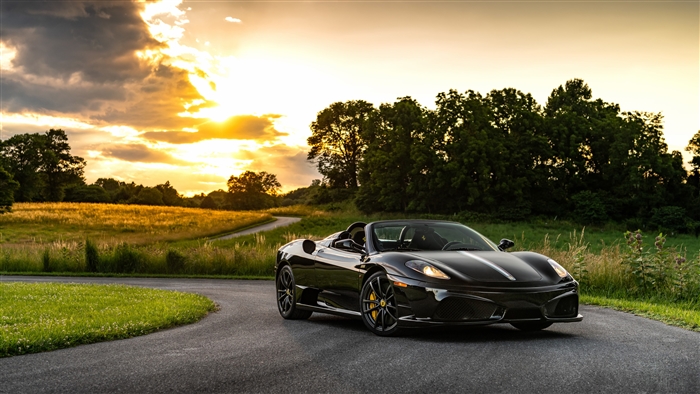 Black Ferrari Scuderia Spider convertible on a road at sunset