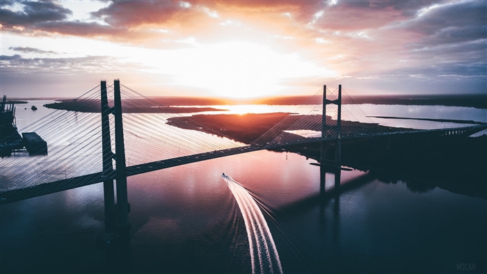 Cable-stayed bridge over river at sunset with boat