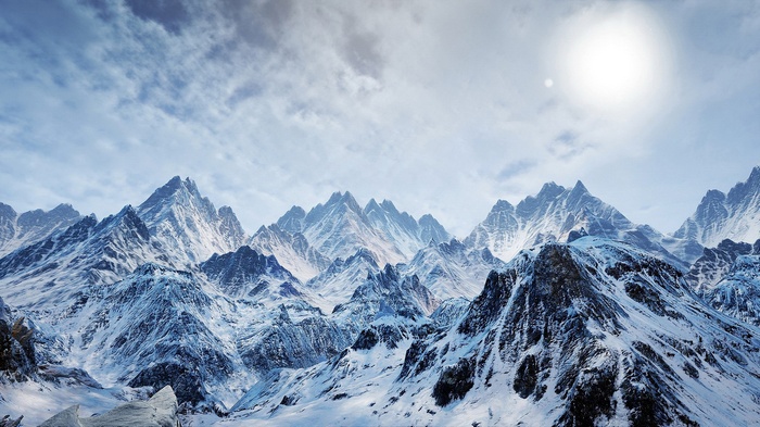 Snow-covered mountains under a bright sun and cloudy sky