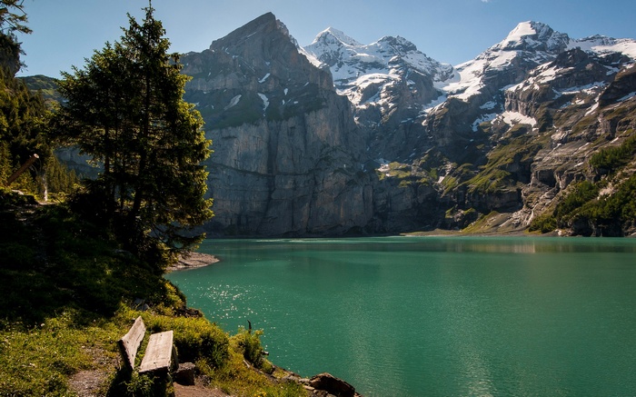 Turquoise lake and snow-capped mountains with trees and bench