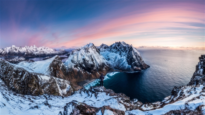 Man on snowy mountain overlooking Norway coast at sunrise