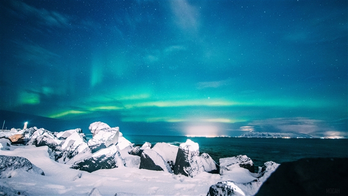 Northern Lights over snowy rocks and ocean