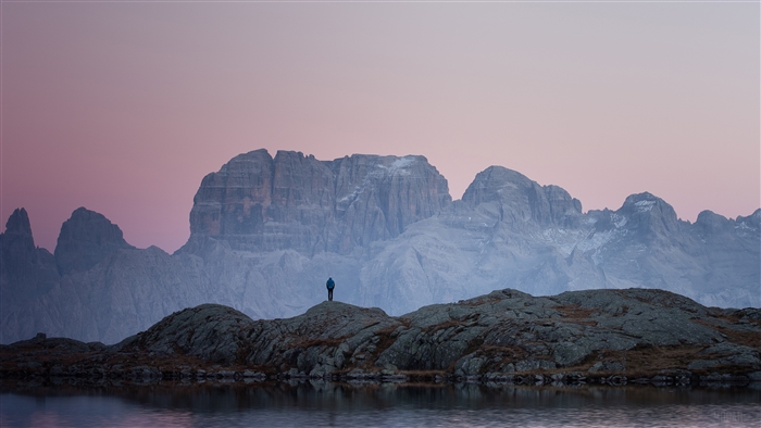 Person standing on rocks overlooking mountains at sunset 4K