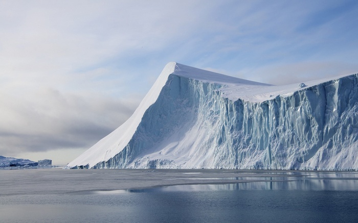 Massive glacier calving into the ocean under a cloudy sky