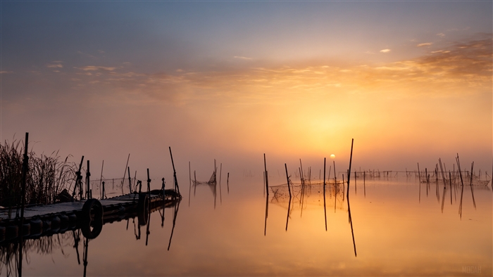 Sunset over a misty lake with fishing nets and a pier