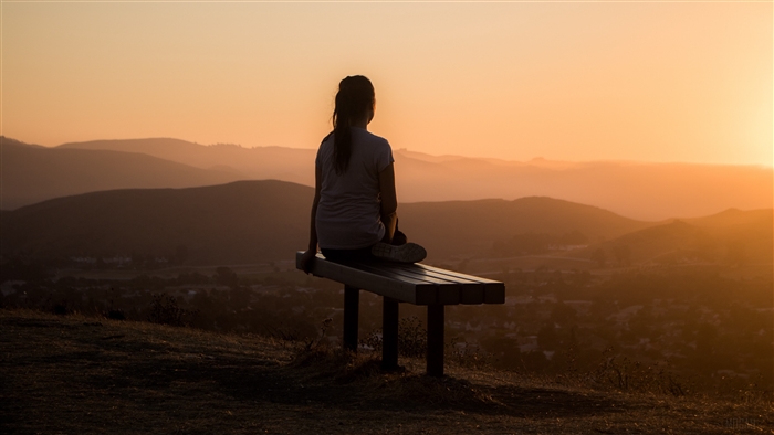 Girl sitting on a bench at sunset overlooking mountains