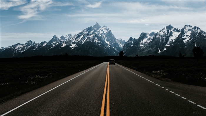 Car on Road Towards Snow-Capped Mountains