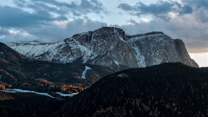 Snow-capped mountains and dark forests under cloudy sky 4K