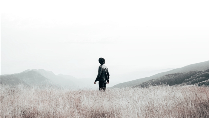Man in hat standing in a field with mountains