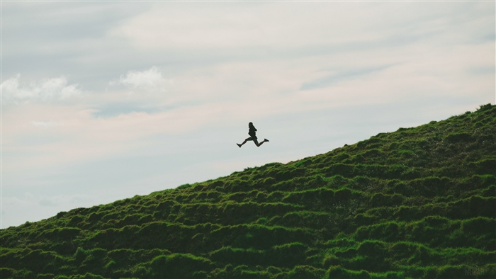 Silhouette of a person jumping on a grassy hill