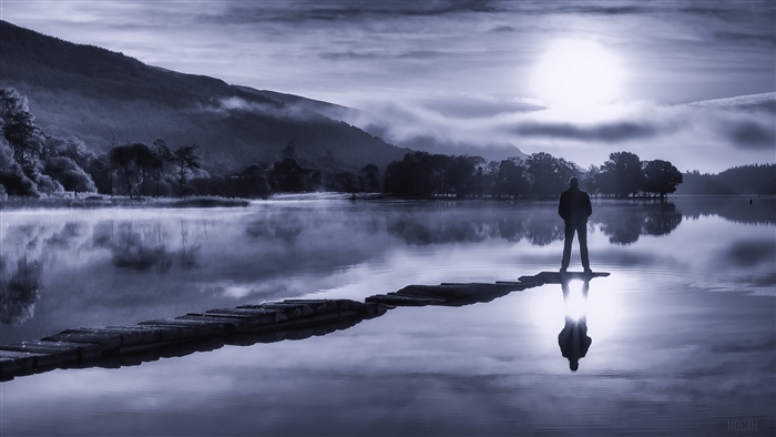 Silhouette of a person on a lake with fog and mountains