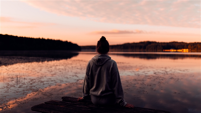 Girl on dock watching sunset over lake 4K