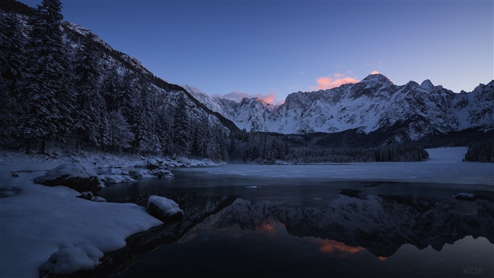 Snowy mountains reflected in a frozen lake at sunrise