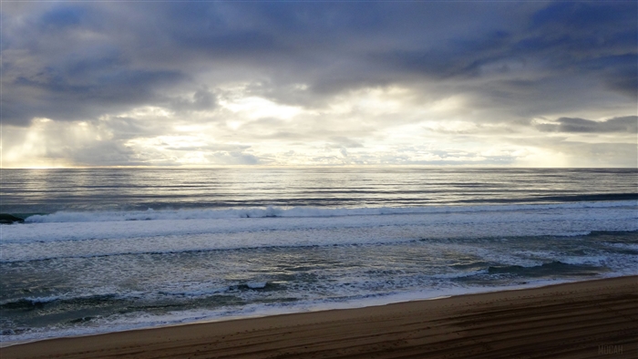 Atlantic Ocean waves crashing on a sandy beach under a cloudy sky