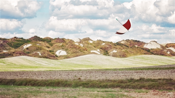 Red and white umbrella flying over rolling hills