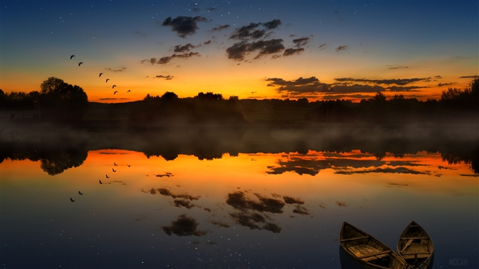 Boats on a lake at sunset with birds flying