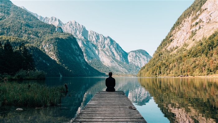 Person sitting on a pier overlooking a lake and mountains