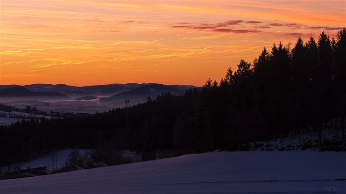 Sunset over snowy hills with forest and valley