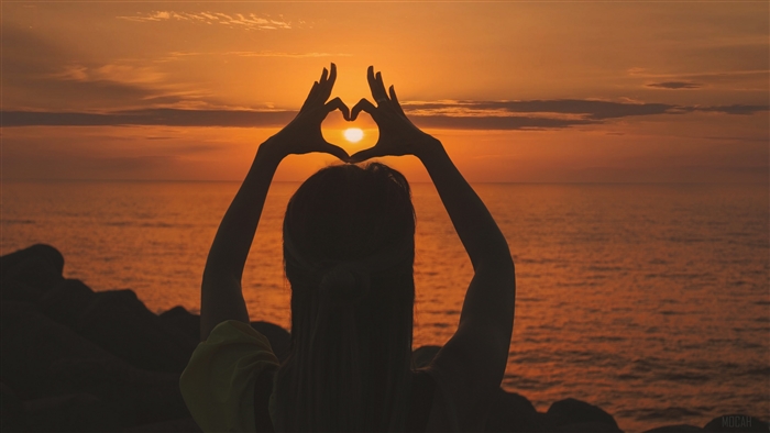 Silhouette of a person making a heart shape at sunset
