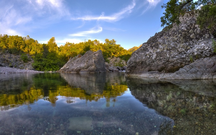 River flowing between rocks and trees under a blue sky