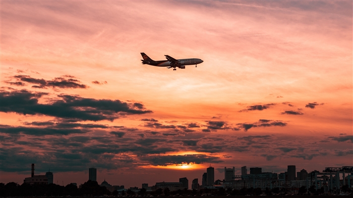 Airplane flying over city skyline at sunset