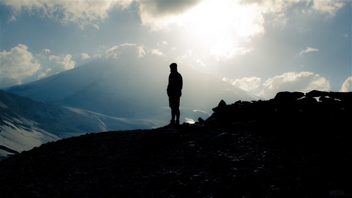 Silhouette of a person on a mountain with Mount Elbrus in the background