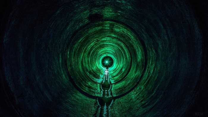 Person walking through a dark green tunnel with light