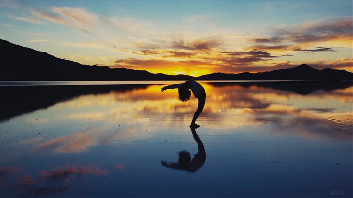Silhouette of a person doing yoga on a lake at sunset