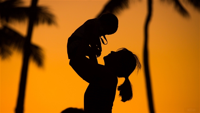 Mother holding child at sunset with palm trees